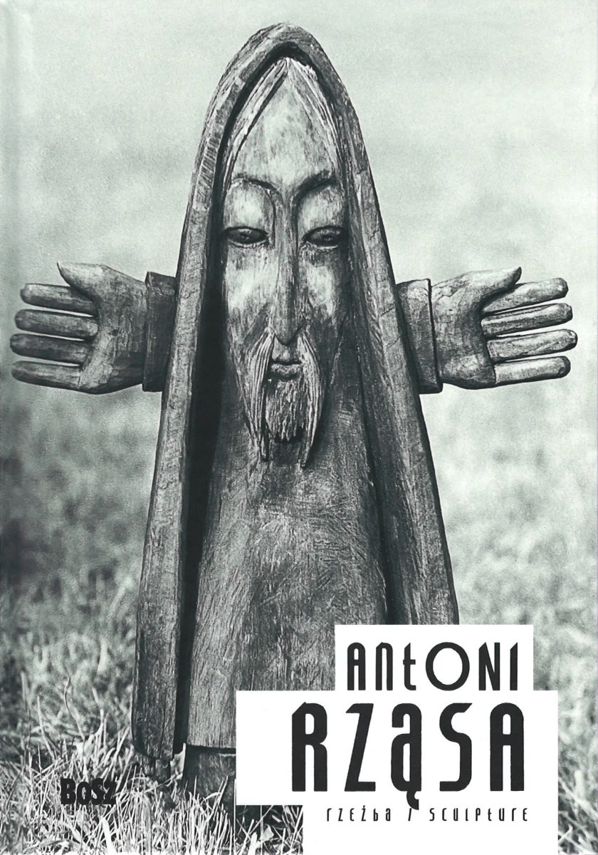 Na okładce widoczna jest drewniana rzeźba stojąca na trawniku przedstawiająca postać skrzata