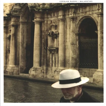 Okładka przedstawia starszego mężczyznę w białym kapeluszu na tle zabytkowej, kamiennej fasady z kolumnami i łukami