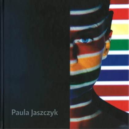 Po prawej stronie okładki widnieje wizerunek autorki w kolorowych, poziomych pasach, lewa strona, utrzymana jest w ciemnej tonacji