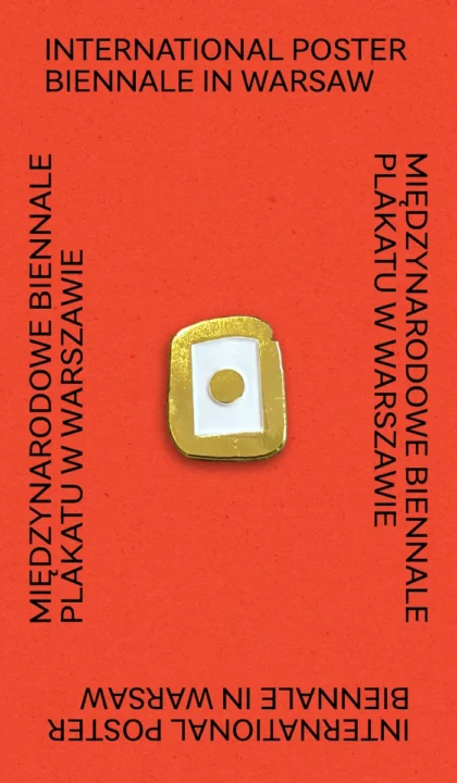 Złoto-biała przypinka w kształcie logo Biennale na czerwonym tle